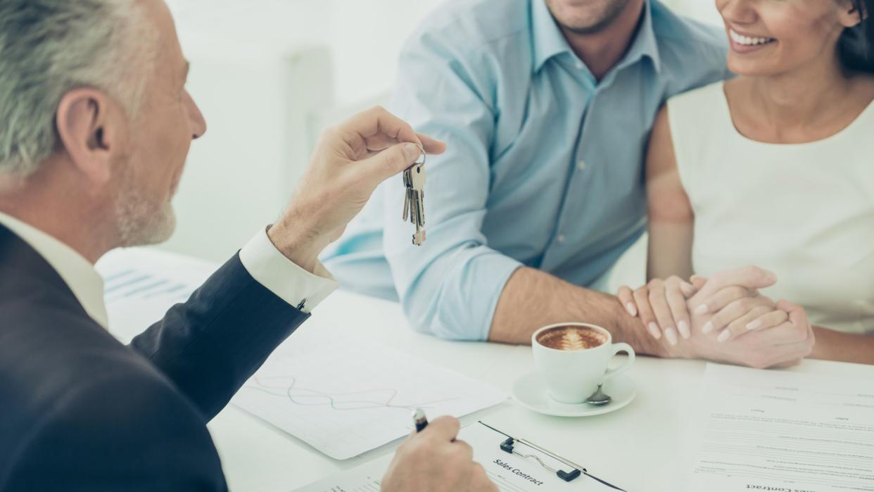 Close up of real estate agent giving keys to couple of customers.