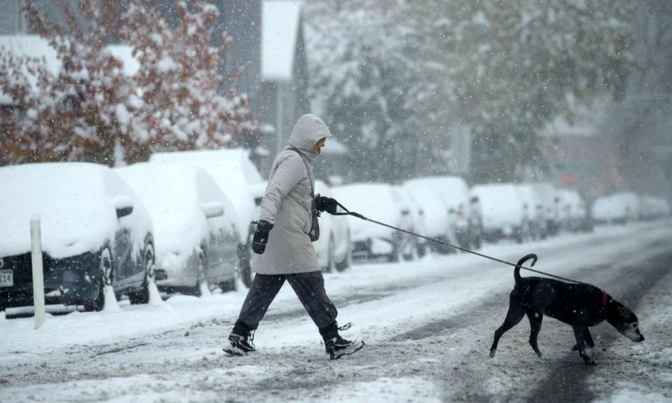 PHOTO: A woman walks a dog across Galapago Street as a winter storm sweeps over Colorado's Front Range communities, Oct. 29, 2023, in Denver. (David Zalubowski/AP)