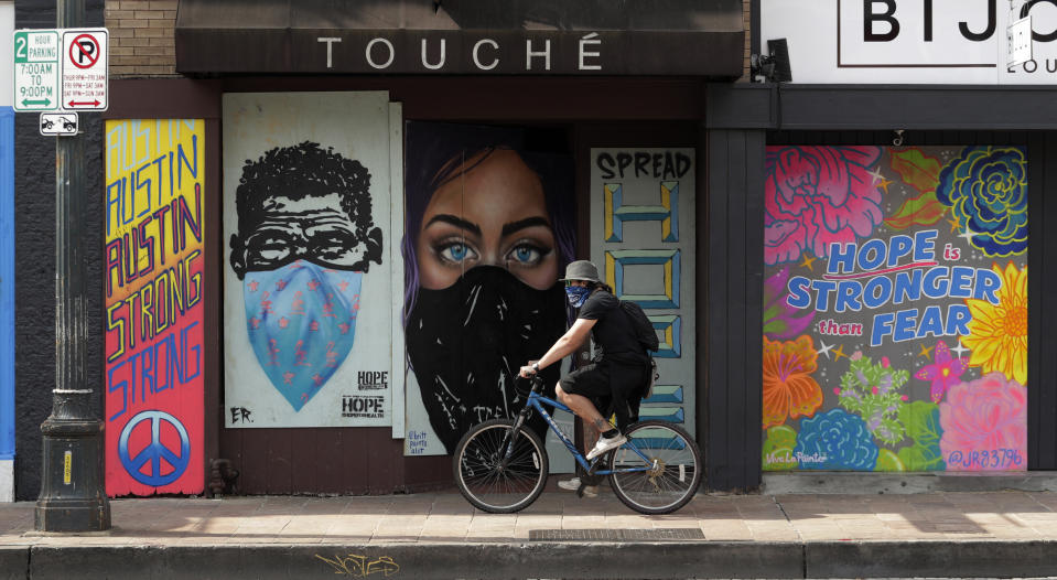 FILE - In this April 6, 2020, file photo, a cyclist wears a bandana over his face as he travels past a boarded up business in downtown Austin, Texas. The coronavirus crisis is upending service businesses, and the crisis may permanently change the way Americans work, shop and socialize, even after the disease fades away. (AP Photo/Eric Gay, File)