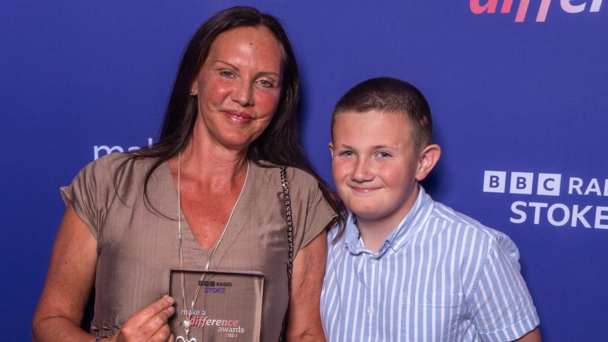 A woman holding an award stood next to a boy in a blue and white striped shirt