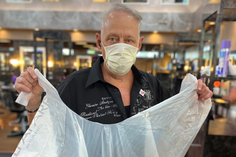 Lester Crowell poses with a disposable smock that the new rules require customers to wear in in Marietta