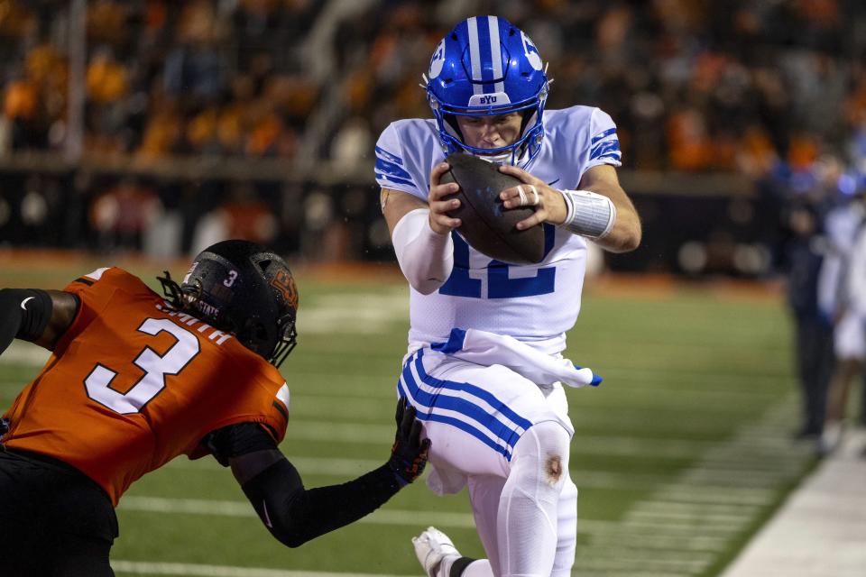 BYU quarterback Jake Retzlaff (12) jumps past Oklahoma State cornerback Cam Smith (3) for a touchdown in overtime of an NCAA college football game Saturday, Nov. 25, 2023, in Stillwater, Okla. | Mitch Alcala, Associated Press