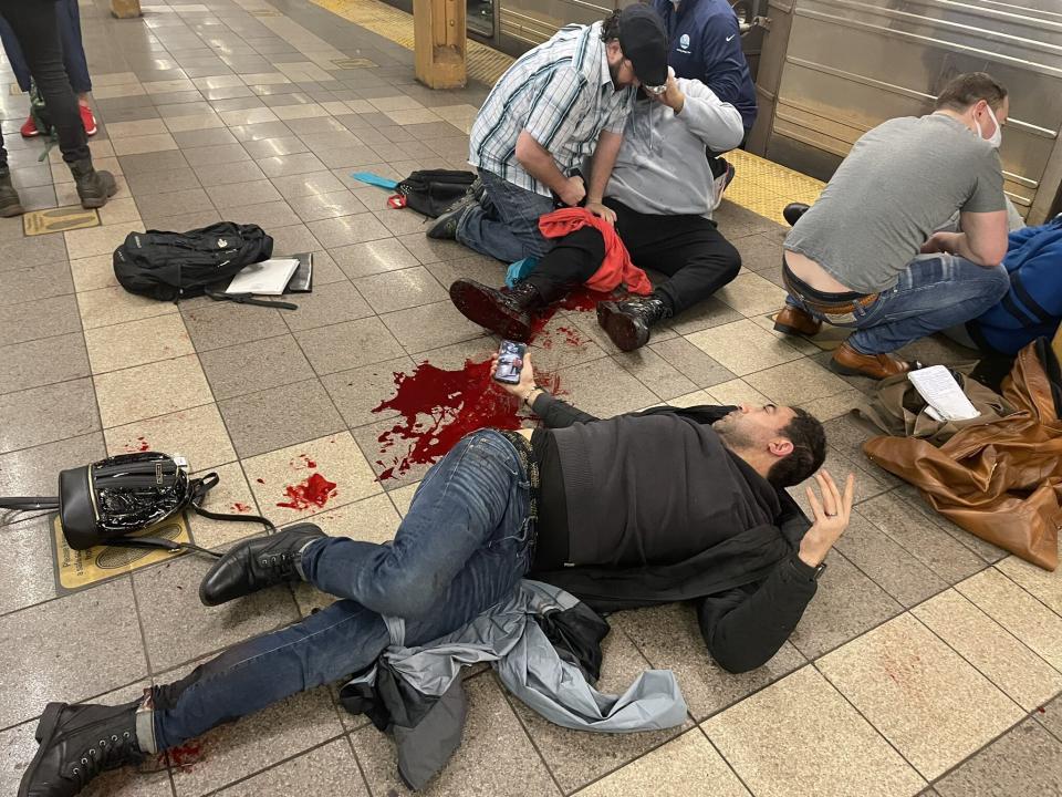 Victims of the shooting on the platform of the subway station, tended to by others, with a pool of blood on the ground.