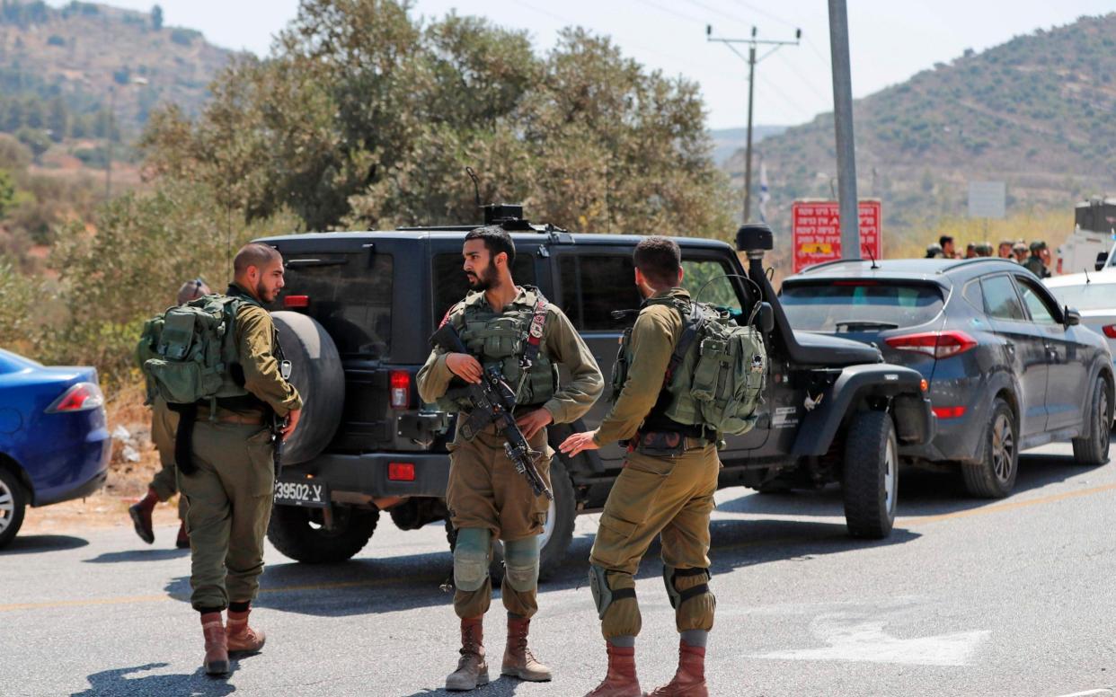 Israeli soldiers stand at the site where a bomb was reportedly thrown from a passing car near the Israeli of Dolev in the occupied West Bank - AFP