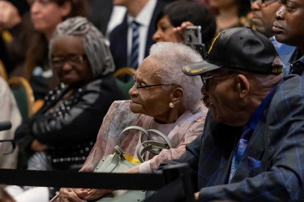 Viola Fletcher, in pink jacket, and Hughes Van Ellis, in U.S. Army cap, sit listening. 