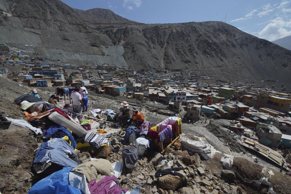 A family sits with belongings recovered from their home destroyed by a landslide, in Camana, Peru, Tuesday, Feb. 7, 2023. Authorities in Peru say landslides triggered by steady rains swept mud, water and rocks into several villages in the country's southern region. (AP Photo/Jose Sotomayor)