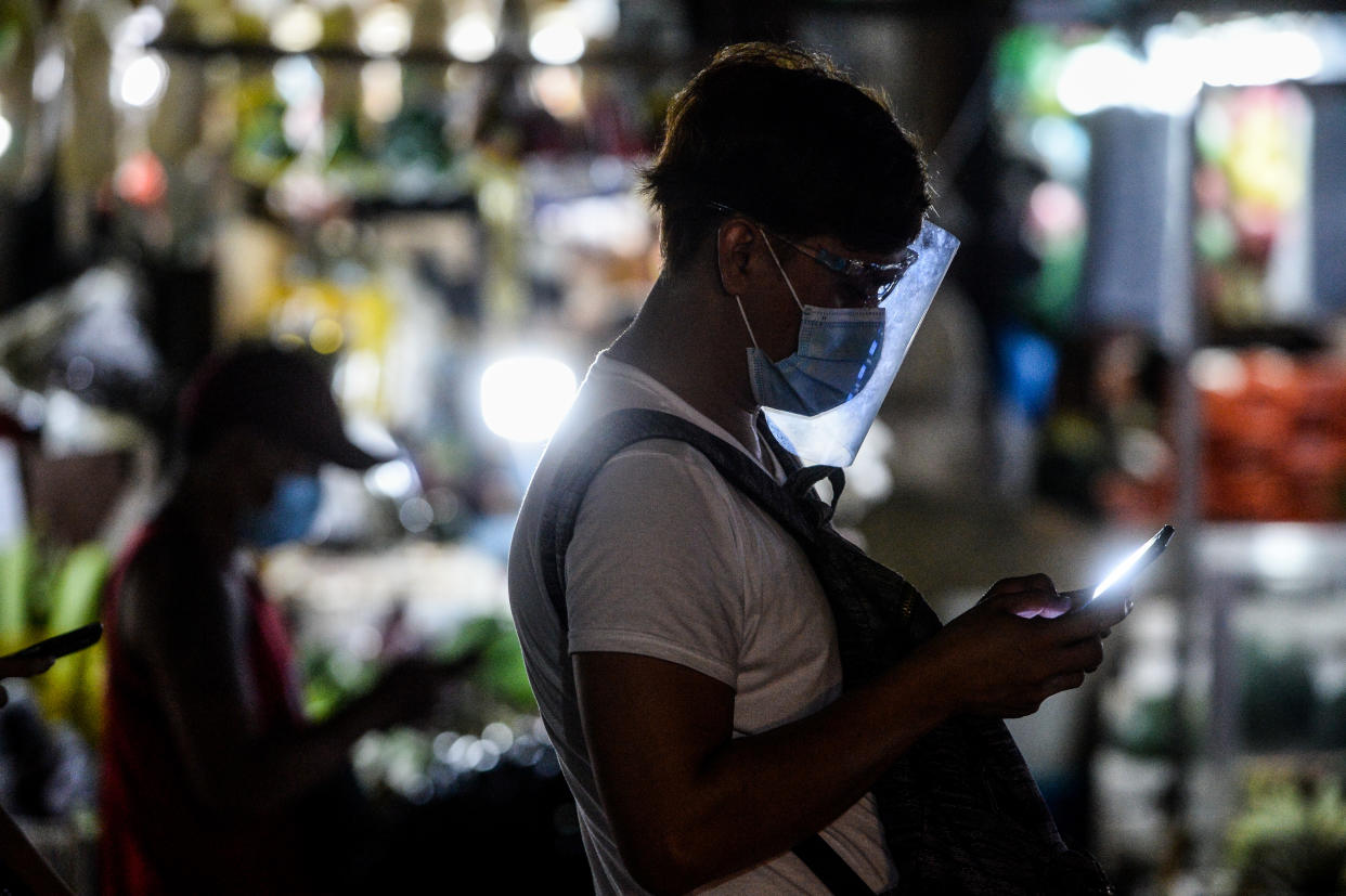 FILE PHOTO: A man wearing a face mask and a face shield uses his smartphone at a bus terminal in Quezon City, Philippines on August 22, 2020. (Photo by Lisa Marie David/NurPhoto via Getty Images)