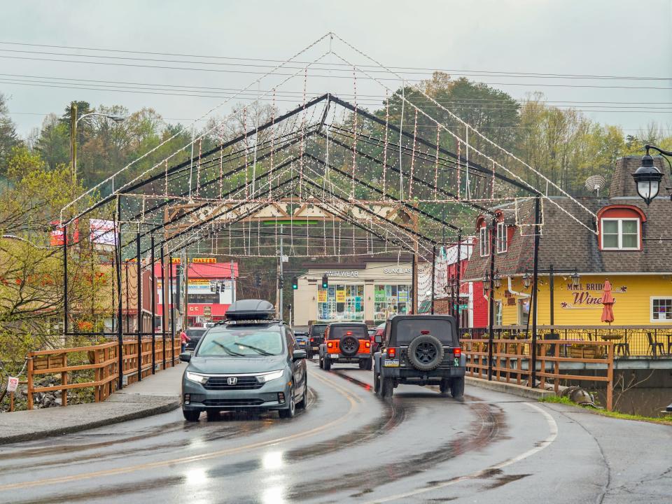 Cars drive in both directions on a bridge with trees and gray skies in the background