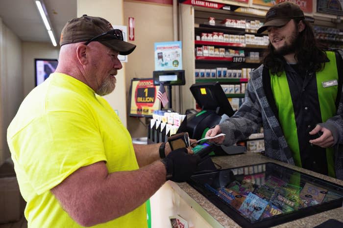 A man buys a lottery ticket from another man behind a counter