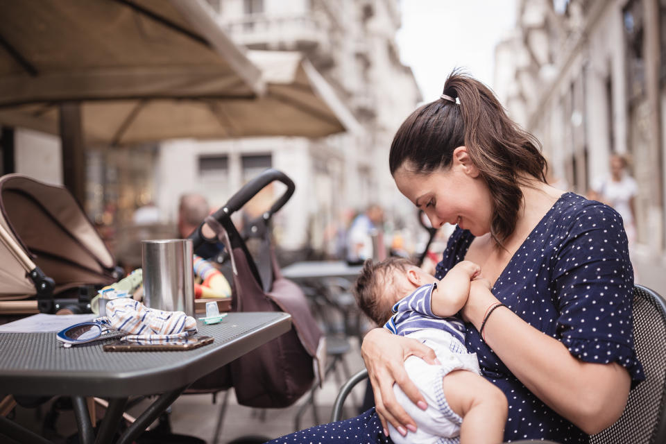 Young mother breastfeeding her baby boy in public place. Trieste, Italy, Europe