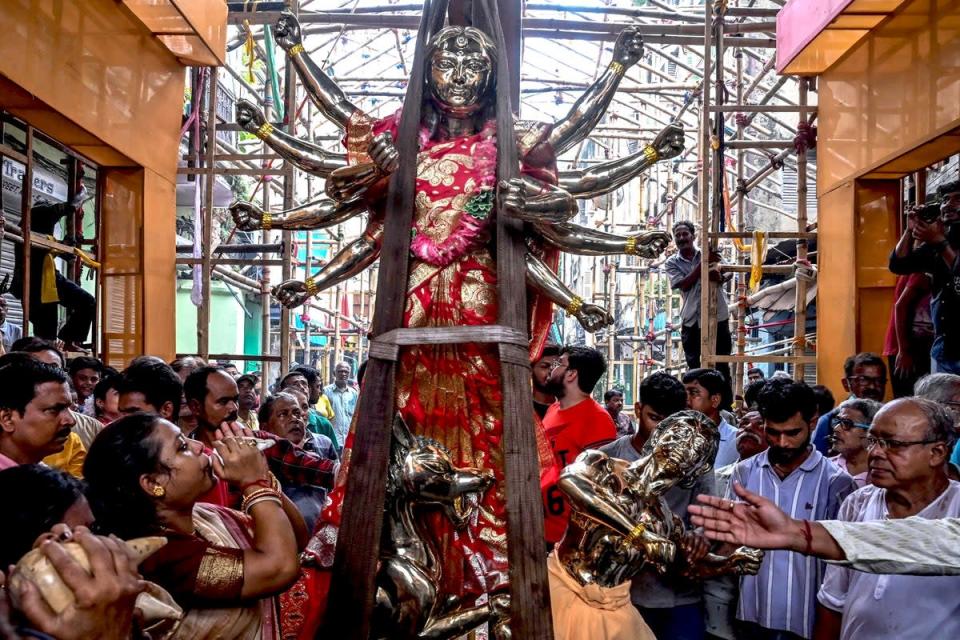 4 de septiembre de 2022: los devotos se reúnen cerca de un ídolo de la diosa hindú Durga, que pesa alrededor de una tonelada métrica, mientras una grúa lo coloca dentro de una estructura fabricada antes del festival Durga Puja en Calcuta (AFP/Getty)