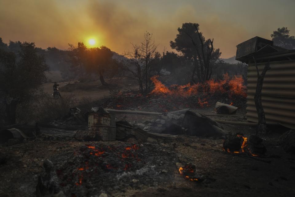 A man on a motorcycle looks at a shipyard which is on fire in Mandra west of Athens, on Tuesday, July 18, 2023. (AP Photo/Petros Giannakouris)