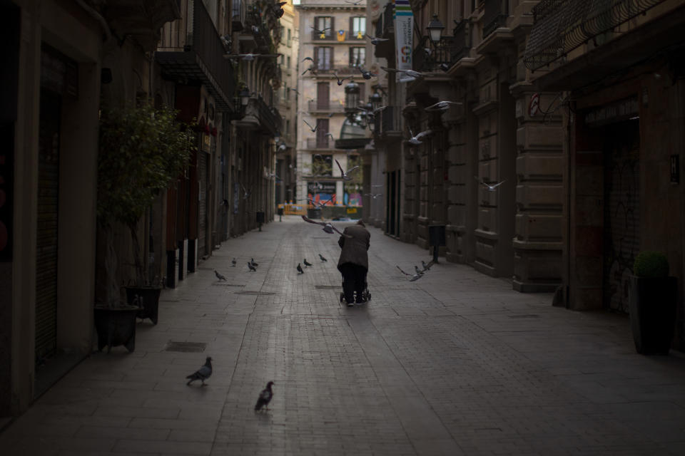In this Saturday, March 21, 2020 photo, a woman pushes a cart with her belongings as she walks along an empty street in downtown Barcelona, Spain. While Spanish authorities tell the public that staying home is the best way to beat the coronavirus pandemic, some people are staying out because home has come to mean the streets of Madrid and Barcelona. (AP Photo/Emilio Morenatti)