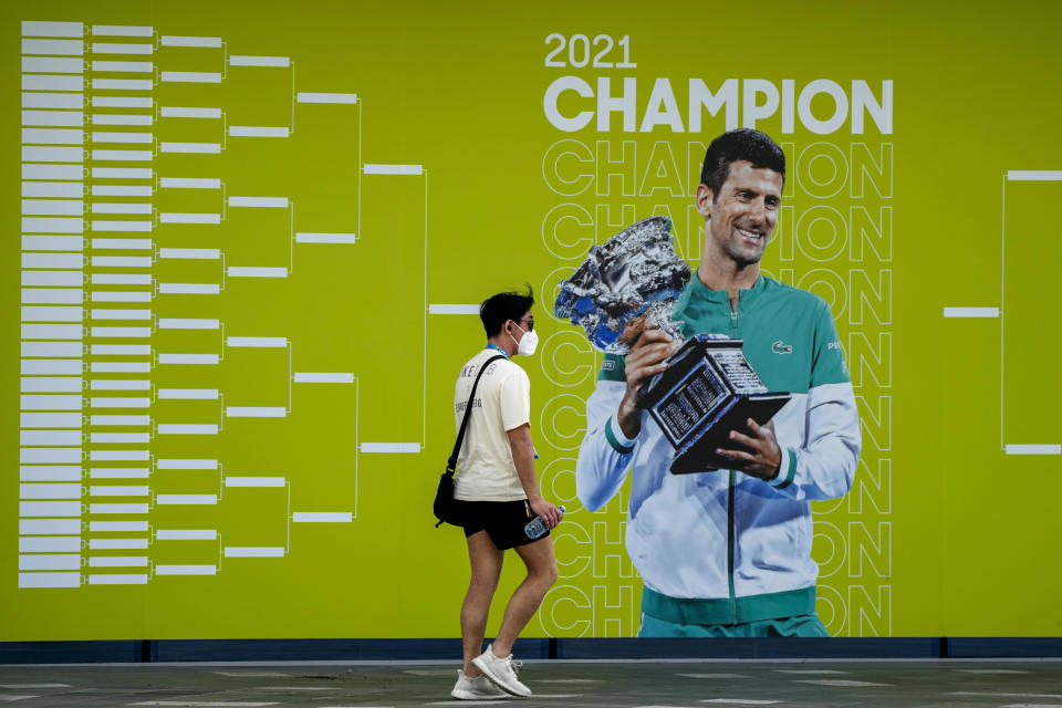 FILE - A man walks past a billboard featuring defending champion, Serbia's Novak Djokovic, ahead of the Australian Open at Melbourne Park in Melbourne, Australia, Tuesday, Jan. 11, 2022. Weary after two years of some of the harshest COVID-19 border restrictions in the world, many Australians wanted Djokovic kicked out of their country for traveling to the tennis tournament without being vaccinated. But the backdrop to the government's tough line on the defending Australian Open champion and Prime Minister Scott Morrison’s description of the expulsion as a "decision to keep our borders strong" dates to nearly a decade ago. It also shines a light on Australia's complicated, and strongly criticized, immigration and border policies. (AP Photo/Mark Baker, File)