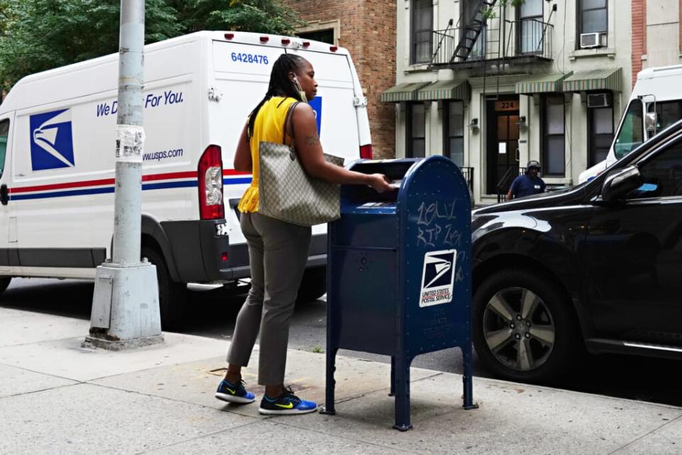 A woman wearing a protective mask at her chin uses a USPS mailbox as the city continues Phase 4 of re-opening following restrictions imposed to slow the spread of coronavirus on August 17, 2020 in New York City. (Photo by Cindy Ord/Getty Images)