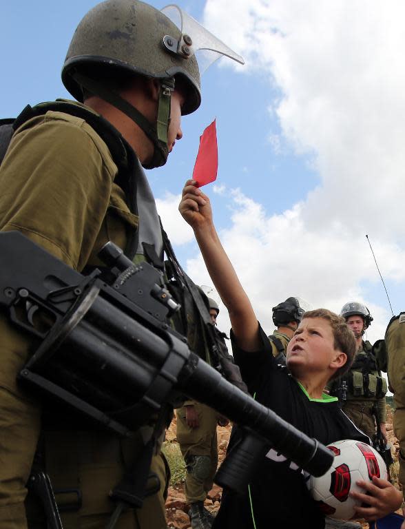 A Palestinian boy shows a red card to an Israeli soldier during a rally to show their support for the Palestinian bid to vote the Israel Football Association (IFA) out of FIFA