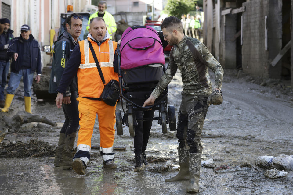 A rescuer helps a woman after heavy rainfall triggered landslides that collapsed buildings and left as many as 12 people missing, in Casamicciola, on the southern Italian island of Ischia, Sunday, Nov. 27, 2022. Firefighters are working on rescue efforts as reinforcements are being sent from nearby Naples, but are encountering difficulties in reaching the island either by motorboat or helicopter due to the weather. (AP Photo/Salvatore Laporta)