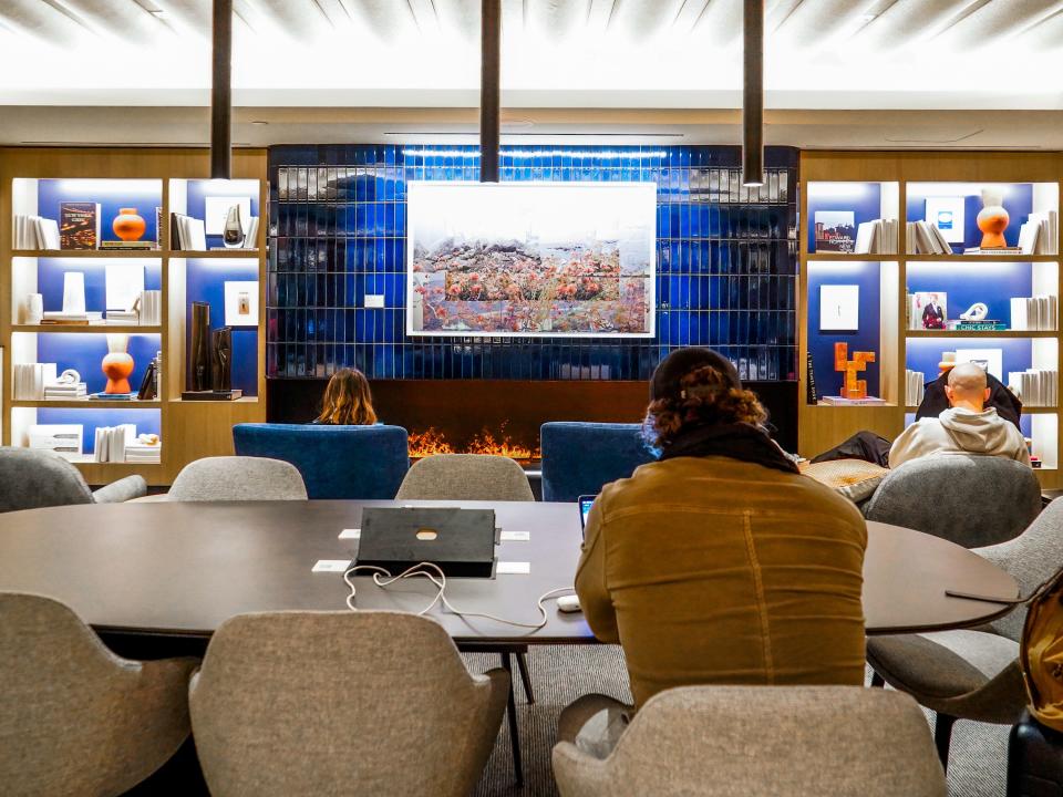 People sit facing away from the camera in a study space with an electric fireplace below a blue-tiled wall