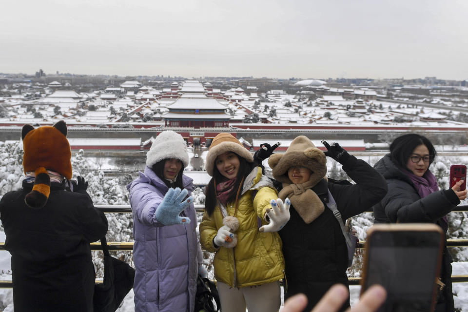 En esta imagen, distribuida por la agencia noticiosa estatal de China, Xinhua, visitantes posan para una foto con la Ciudad Prohibida y el parque Jingshan de fondo, tras una intensa nevada, en Beijing, el 21 de febrero de 2024. (Ju Huanzong/Xinhua vía AP)