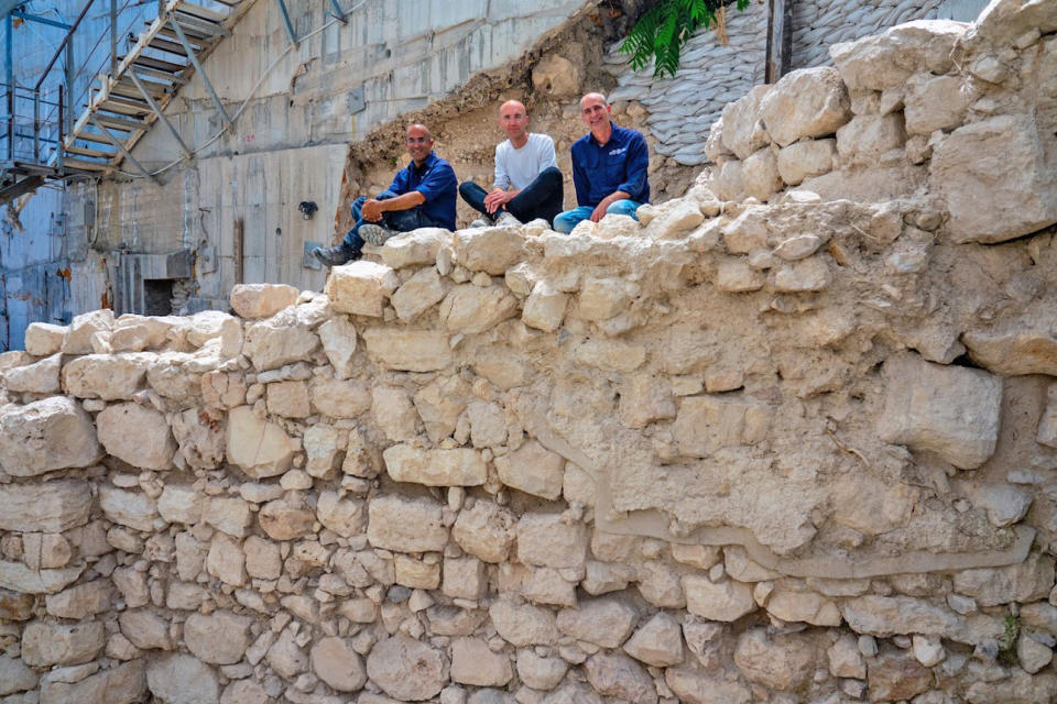 Three men sit on top of an ancient stone wall.