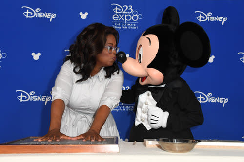 <p>Disney’s rodent-in-chief smooches Oprah while her handprints are preserved. (Photo: Disney) </p>