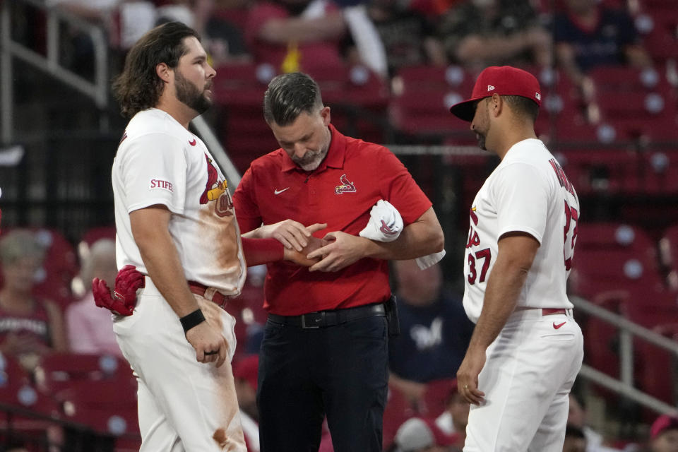 St. Louis Cardinals first baseman Alec Burleson, left, is checked by trainer Adam Olsen as manager Oliver Marmol (37) watches after being injured sliding into third during the first inning of a baseball game against the Milwaukee Brewers Tuesday, Sept. 19, 2023, in St. Louis. (AP Photo/Jeff Roberson)
