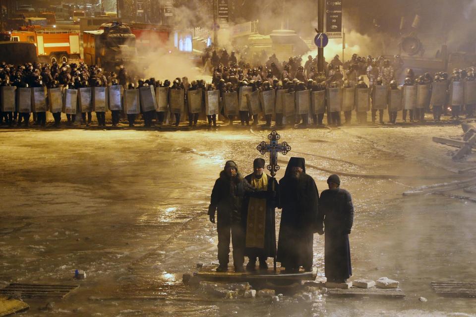 FILE In this file photo taken on Friday, Jan. 24, 2014, Orthodox priests pray as they stand between pro-European Union activists and police lines in central Kiev, Ukraine. As a barricade of blazing tires belched thick black smoke, a line of priests stood between angry protesters and ominous riot police. Every freezing morning, priests sing prayers to demonstrators gathered on the Ukrainian capital's main square, a solemn and soothing interlude to vehement speeches calling for revolution. (AP Photo/Sergei Grits, file)