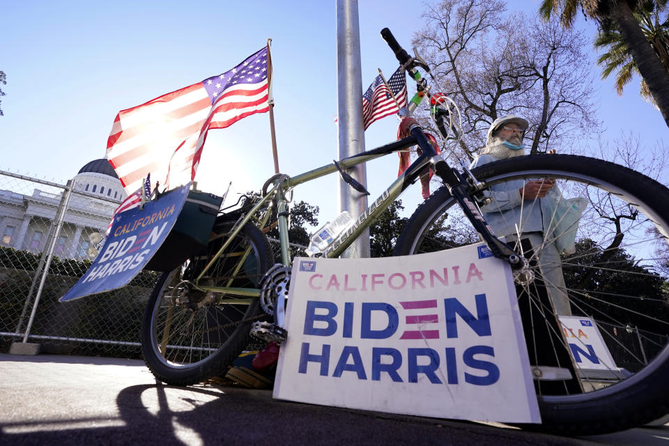 The American flag waves in the wind as a person shows his support for President-elect Joe Biden and Vice President-elect Kamala Harris outside the California state Capitol in Sacramento, Calif., Tuesday, Jan. 19, 2021. (AP Photo/Rich Pedroncelli)