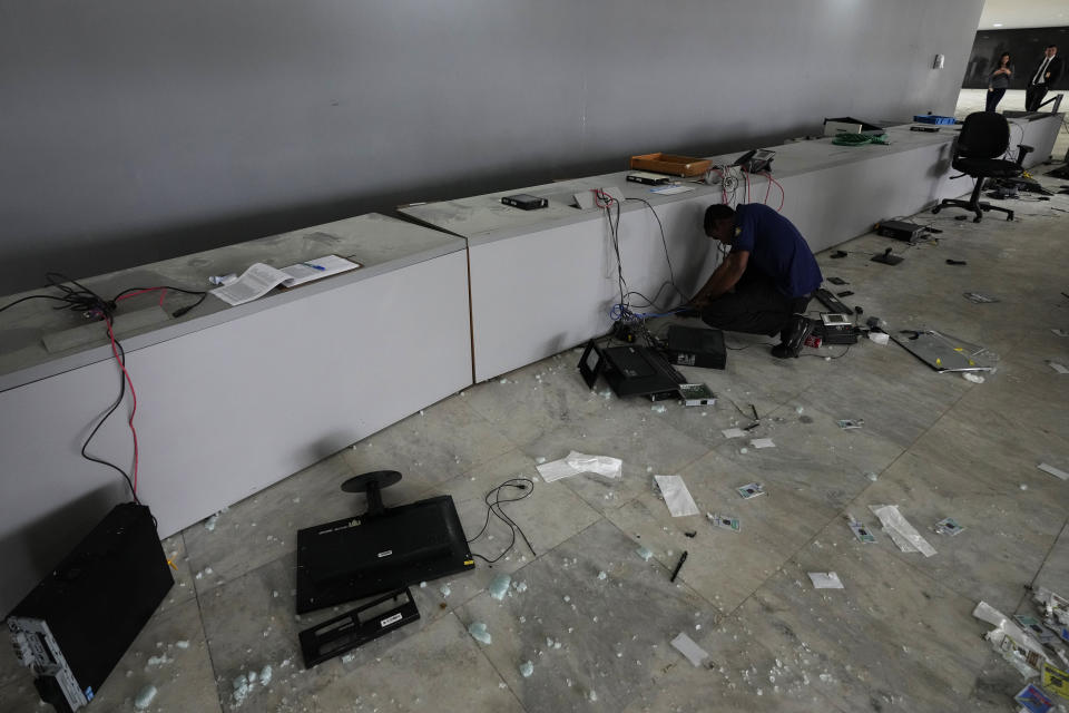 A worker inspects destroyed computers in the main entrance of Planalto Palace, the office of the president, the day after it was stormed by supporters of Brazil's former President Jair Bolsonaro in Brasilia, Brazil, Monday, Jan. 9, 2023. The protesters also stormed Congress and the Supreme Court. (AP Photo/Eraldo Peres)