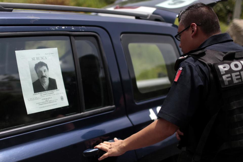 Un policía federal, junto a uno de los coches del cuerpo con una fotografía del narcotraficante fugitivo Joaquín &quot;El Chapo&quot; Guzmán en una carretera entre Ciudad de México y Acapulco el 14 de julio de 2015 (AFP | Pedro PARDO)