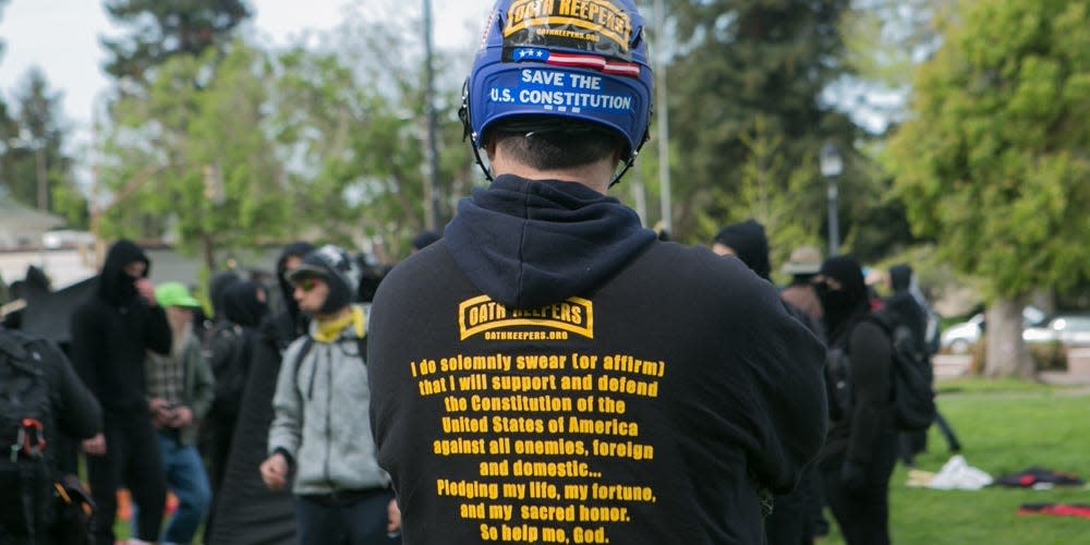 back of Oath Keepers member wearing a helmet and hoodie with text about defending the constitution
