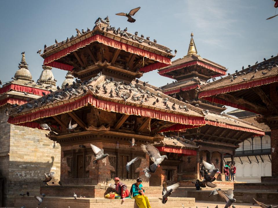 Birds surrounding a monument with people sitting at the base of the structure.