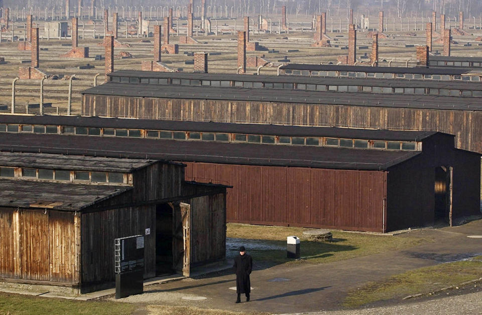 FILE - In this Jan. 17, 2005 file photo, a visitor walks by the wooden barracks in the former Auschwitz-Birkenau Nazi death camp in Oswiecim, southern Poland. Police and prosecutors in southern Poland were investigating on Wednesday, Oct. 6, 2021, English and German language graffiti found on the barracks of the former Nazi German death camp of Auschwitz-Birkenau. (AP Photo/Czarek Sokolowski, File)