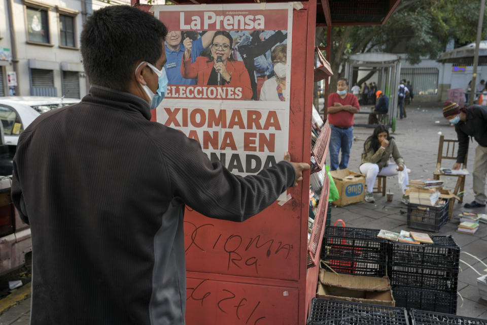 A man sets up his newspaper stand by hanging a poster with a photo of Free Party presidential candidate Xiomara Castro and the day´s headline of her expected victory, after general elections in Tegucigalpa, Honduras, Monday, Nov. 29, 2021. Castro is holding a commanding lead as Hondurans appear poised to remove the conservative National Party after 12 years of continuous rule. (AP Photo/Moises Castillo)