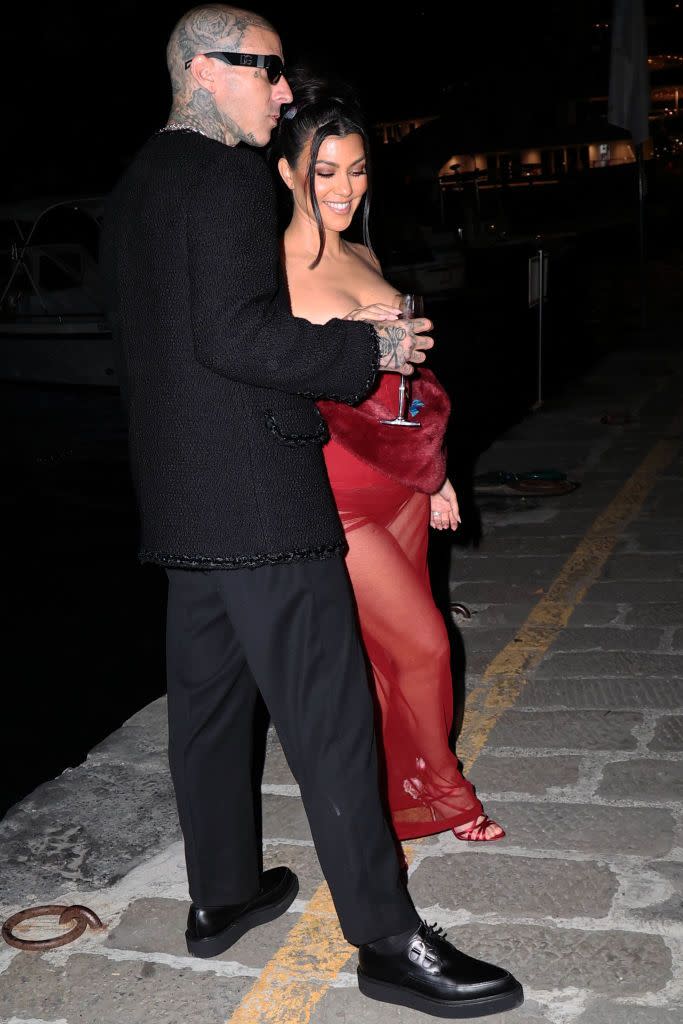 <p>The dresscode for this weekend seems to be "Dolce & Gabbana everything' since that's the brand the woman of the Kardashian-Jenner clan seems to be wearing throughout the snaps from the event. </p><p>Here, Kourtney Kardashian wears a slinky sheer crimson dress with strappy heels and a furry stole. Travis Barker wears a bouclé jacket and simple black trousers. </p>
