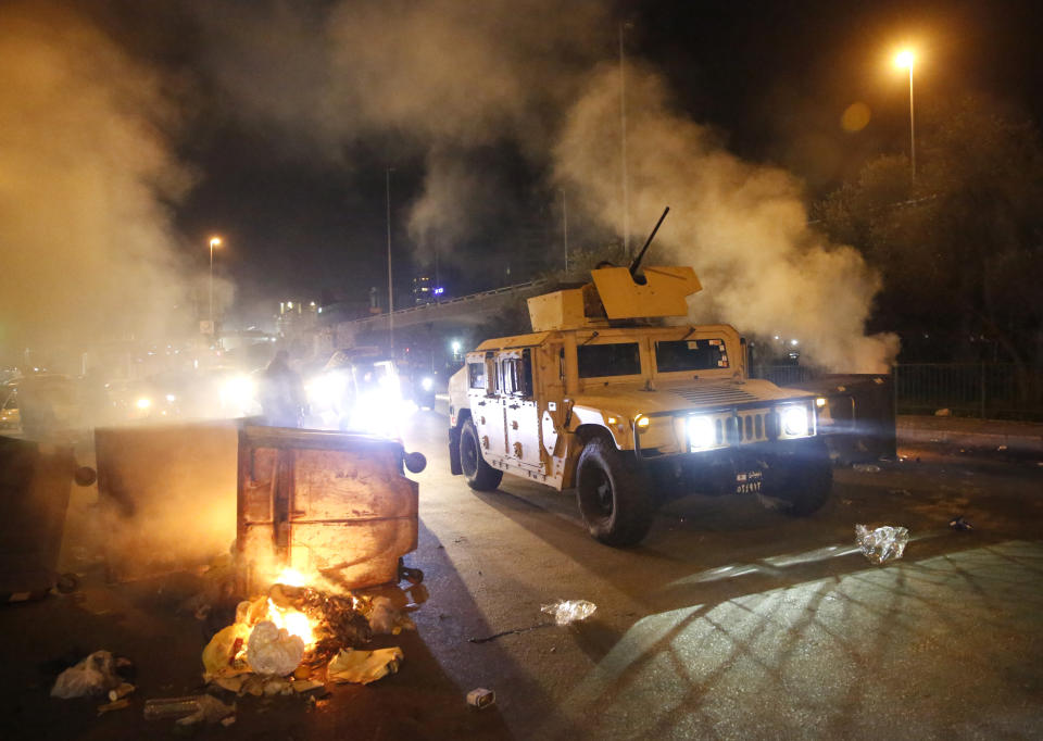 Lebanese army vehicle pass garbage containers that were set on fire by anti-government protesters to block roads in Beirut, Lebanon, Tuesday, Jan. 21, 2020. Lebanon's prime minister designate Hassan Diab announced Tuesday a new government for the crisis-hit country, breaking a months-long impasse amid ongoing mass protests against the country's ruling elite. (AP Photo/Hussein Malla)