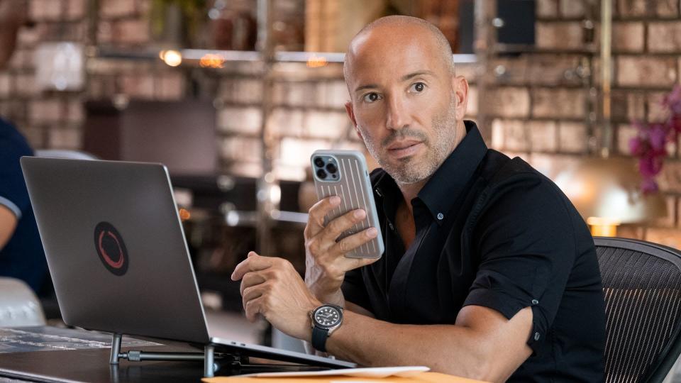 Jason Oppenheim holding a phone as he works at his desk. 