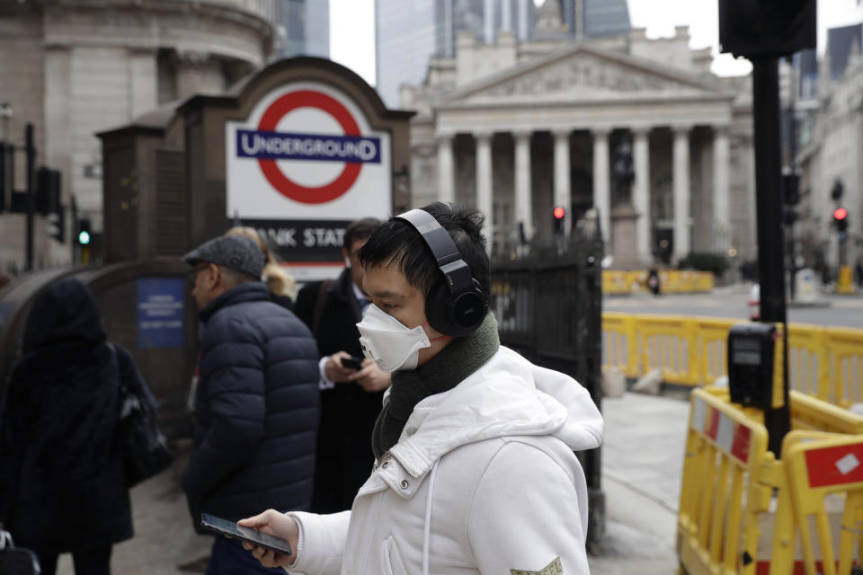 A man wearing a face mask walks past an entrance sign for Bank underground train station backdropped by the Royal Exchange building in London, Wednesday, March 4, 2020. British authorities laid out plans Tuesday to confront a COVID-19 epidemic, saying that the new coronavirus could spread within weeks from a few dozen confirmed cases to millions of infections, with thousands of people in the U.K. at risk of death. (AP Photo/Matt Dunham)