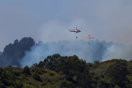 Two helicopters carries water to fight a forest fire seen in the village of Guia