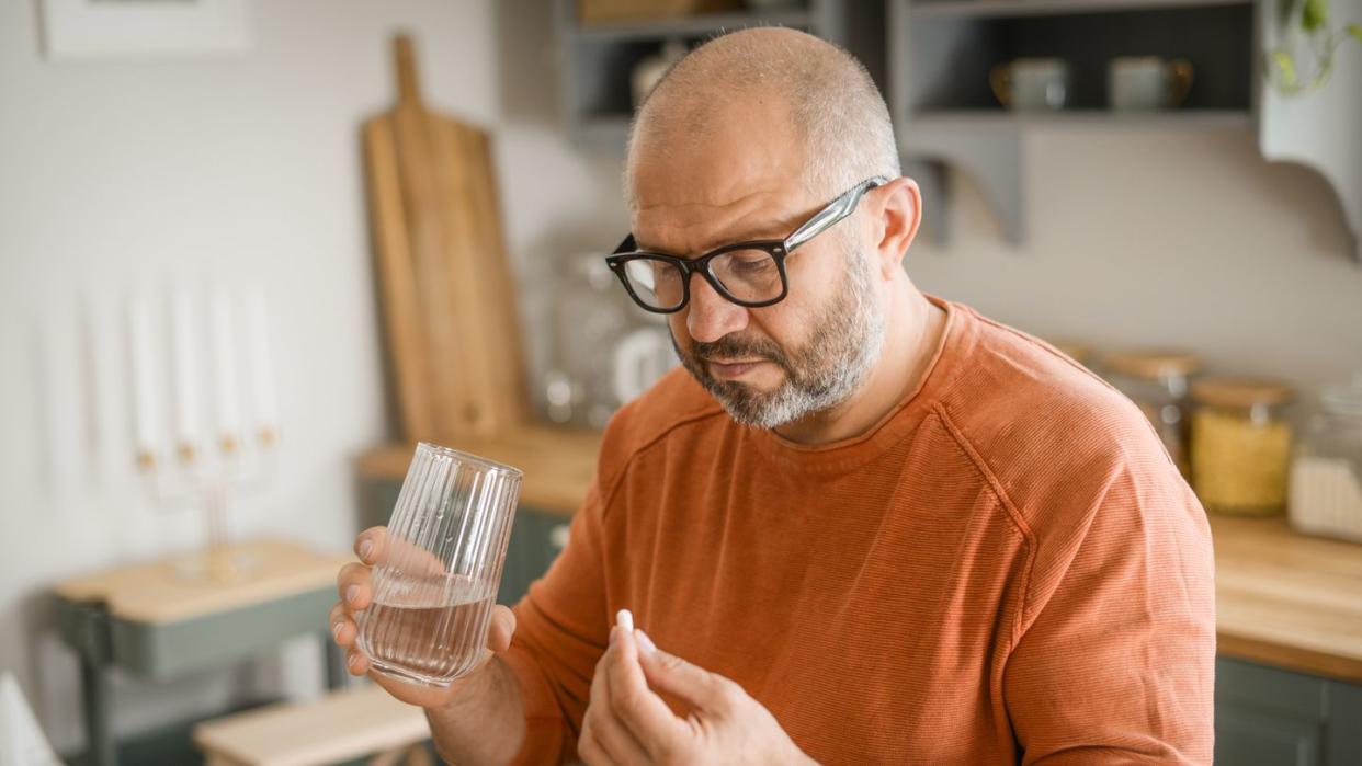 mature adult man in cozy interior of home kitchen  taking medication