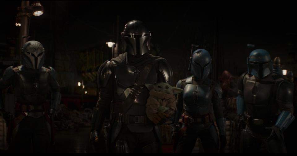 Din Djarin holds Grogu in front of other Mandalorians
