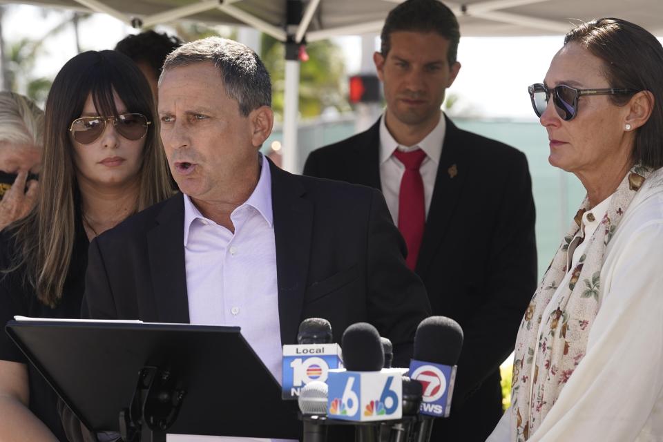 Pablo Langesfeld talks during the unveiling of a large banner with the names of the 98 killed in the Champlain Towers South condominium building collapse, Thursday, May 12, 2022, in Surfside, Fla. Langesfeld lost his daughter Nicole. To the right Ronit Naibryf, lost her son Ilan Naibryft and Chana Wasserman, left, lost her parents Tzvi and Itty Ainsworth. (AP Photo/Marta Lavandier)