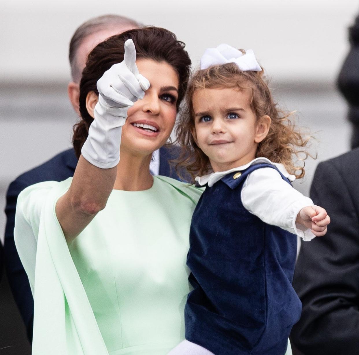 Casey DeSantis points towards the sky while holding her youngest daughter Mamie during the inauguration ceremony for her husband in January 2023.