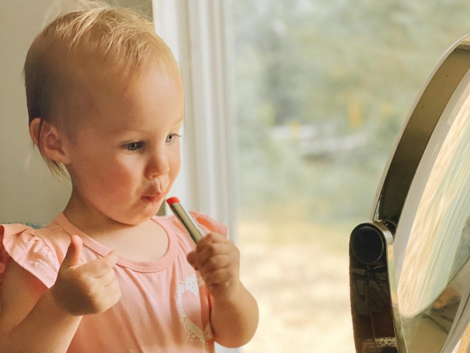 Toddler Autumn McDaid puts on fake, kids' lipstick in front of her mom's mirror