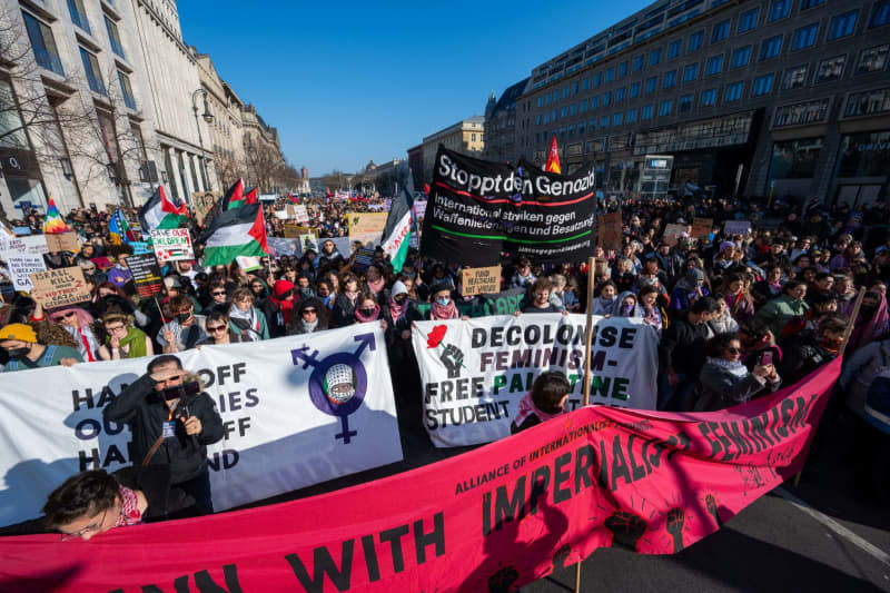 Participants stand on the street Unter den Linden during a demonstration to mark International Women's Day, holding a placard reading "Stop the genocide". Several more demonstrations and rallies are planned in the capital until the evening. Christophe Gateau/dpa