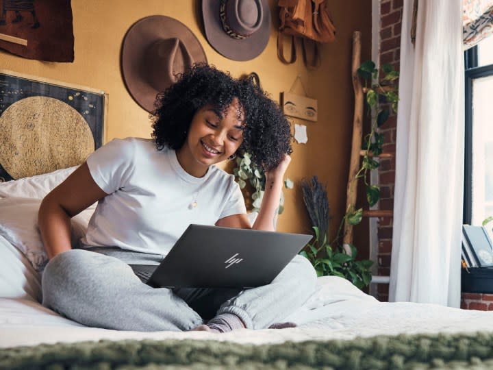 A person using a HP ENVY x360 2-in-1 15.6-inch Touch-Screen Laptop sitting on a bed.