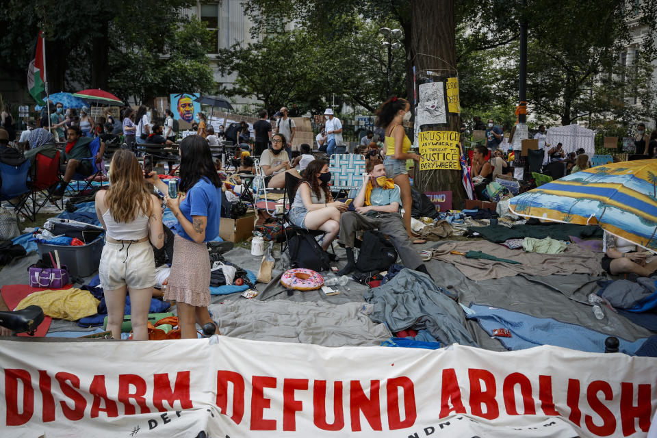 Protesters rest on a grassy area surrounded by signs calling for the changes and abolition of police forces at an encampment outside City Hall, Friday, June 26, 2020, in New York. (AP Photo/John Minchillo)