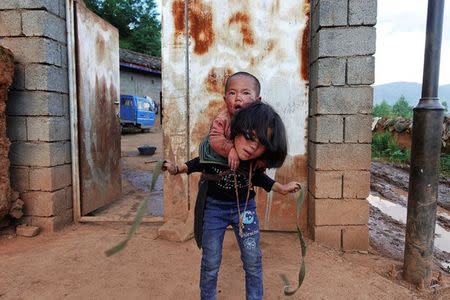 A girl ties a baby onto her back outside a farmhouse on the outskirts of Butuo County, Sichuan province, China July 20, 2017. REUTERS/Natalie Thomas