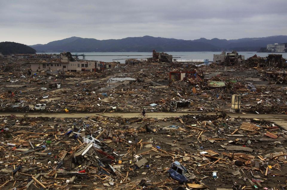 FILE - In this March 15, 2011, file photo, a Japanese survivor of an earthquake and tsunami rides his bicycle through the leveled city of Minamisanriku, Miyagi prefecture, northeastern Japan. March 11, 2021 marks the 10th anniversary of the massive earthquake, tsunami and nuclear disaster that struck Japan's northeastern coast. (AP Photo/David Guttenfelder, File)