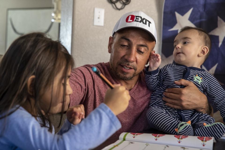 Ronnie Lucero holds his baby son and helps his daughter with schoolwork